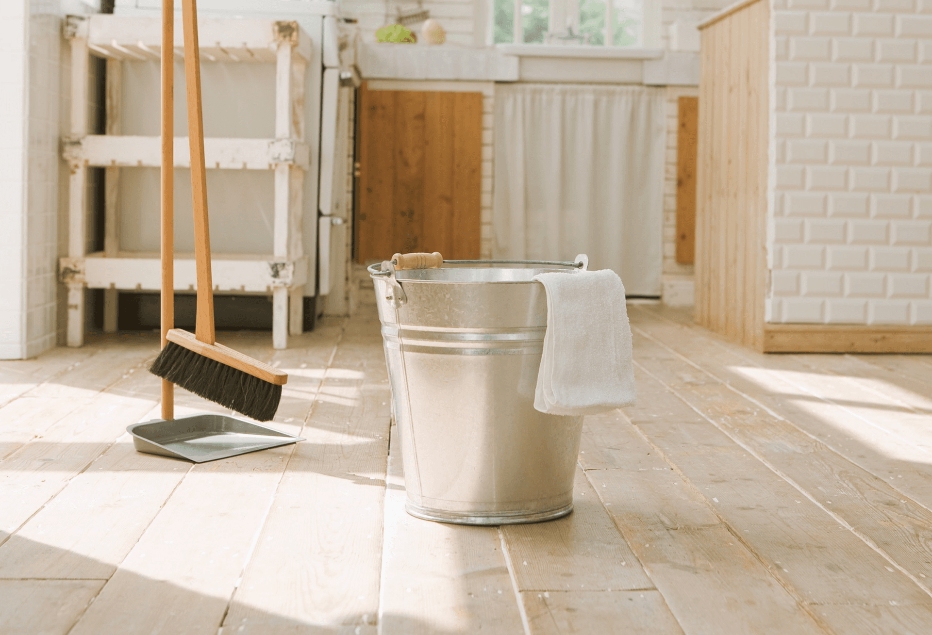 A simple cleaning bucket and broom against a pale wall